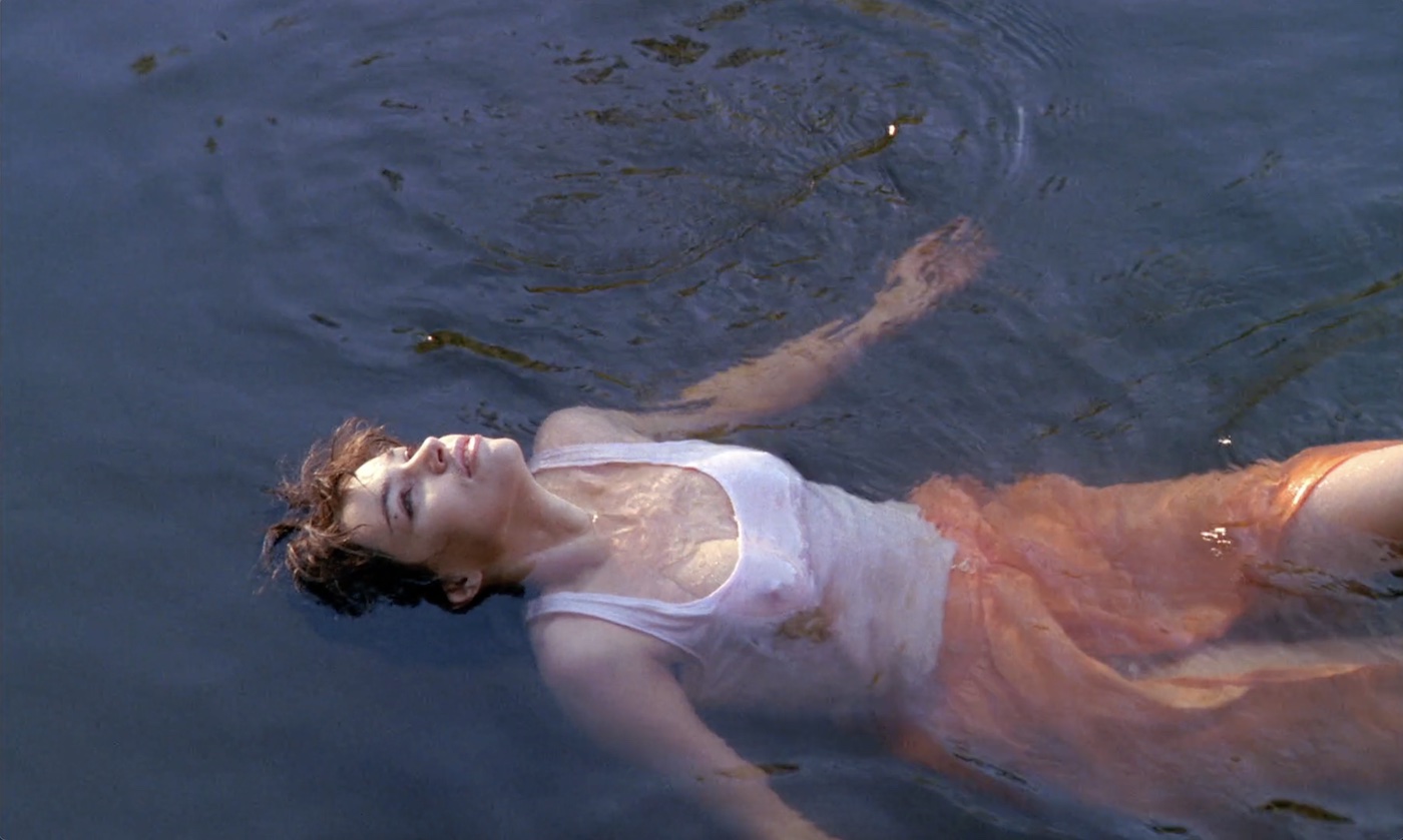 A woman, clothed, floating in a river looking up.