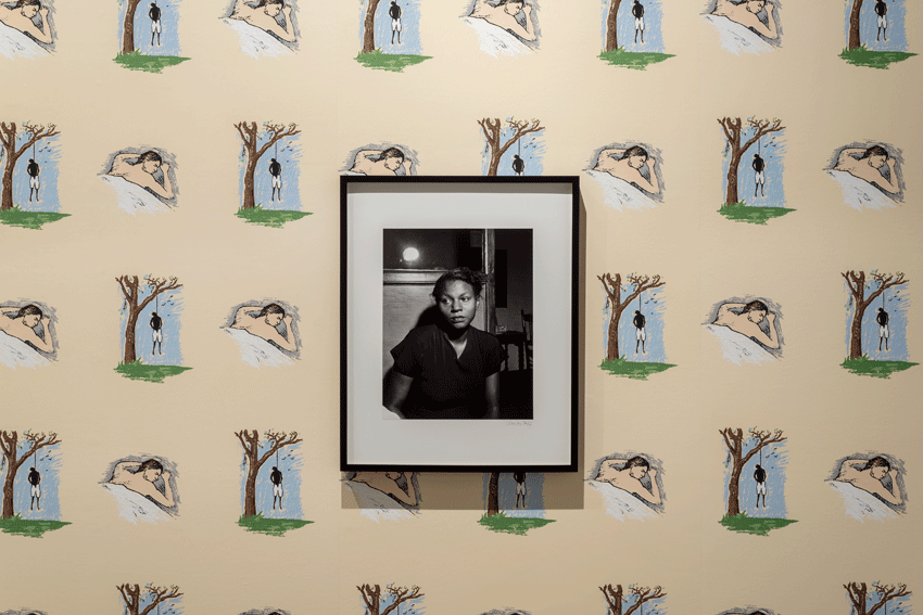 Photograph by Marion Palfi titled 'Wife of a Lynching Victim' hangs on top of wall paper by Robert Gober with drawing of a lynching juxtaposed with drawing of a sleeping white man.