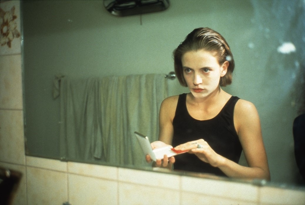 A young woman looking into a bathroom mirror holding a compact in her hand.