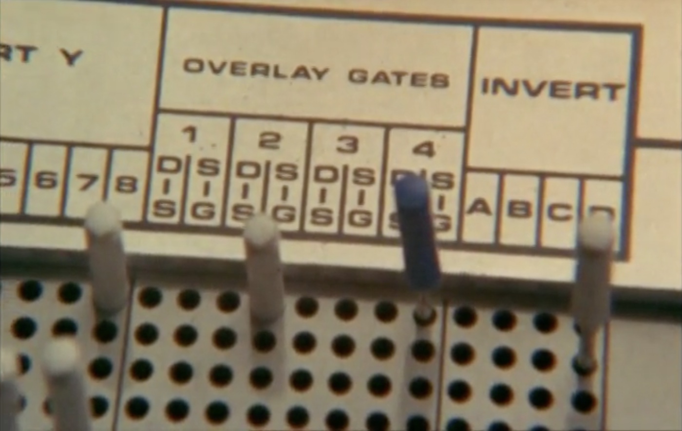 Analog electronic equipment
of some kind with words 'overlay gates' and 'invert' printed above gride of holes, a few filled with pegs.