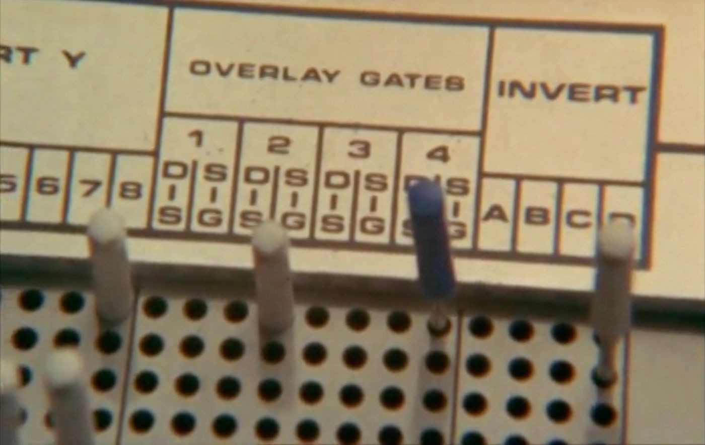 Analog electronic equipment
of some kind with words 'overlay gates' and 'invert' printed above gride of holes, a few filled with pegs.