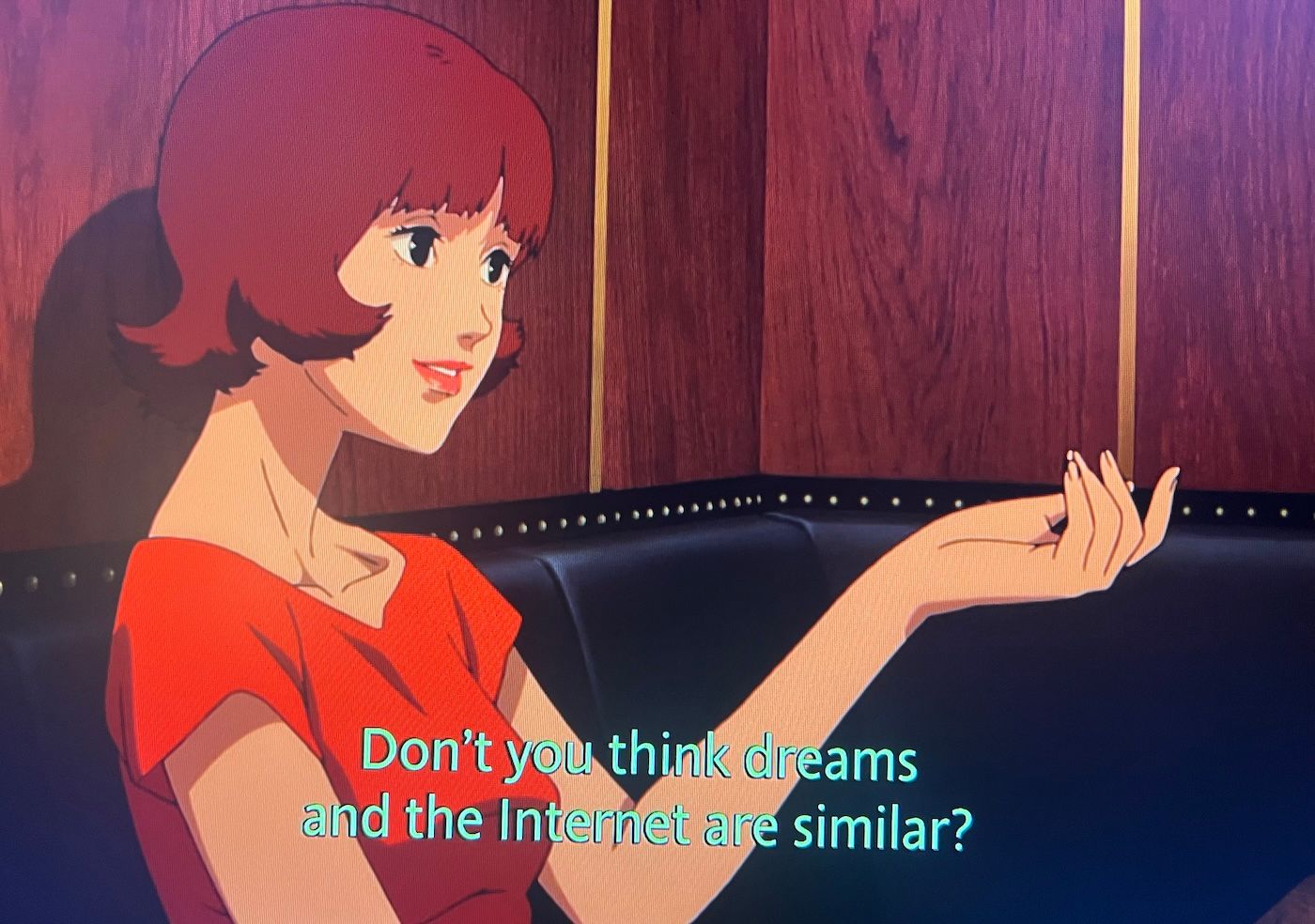 A girl sitting at a table with her hand in the air, drawn in the style of manga. The caption reads 'Don't you think dreams and the internet are similar?'