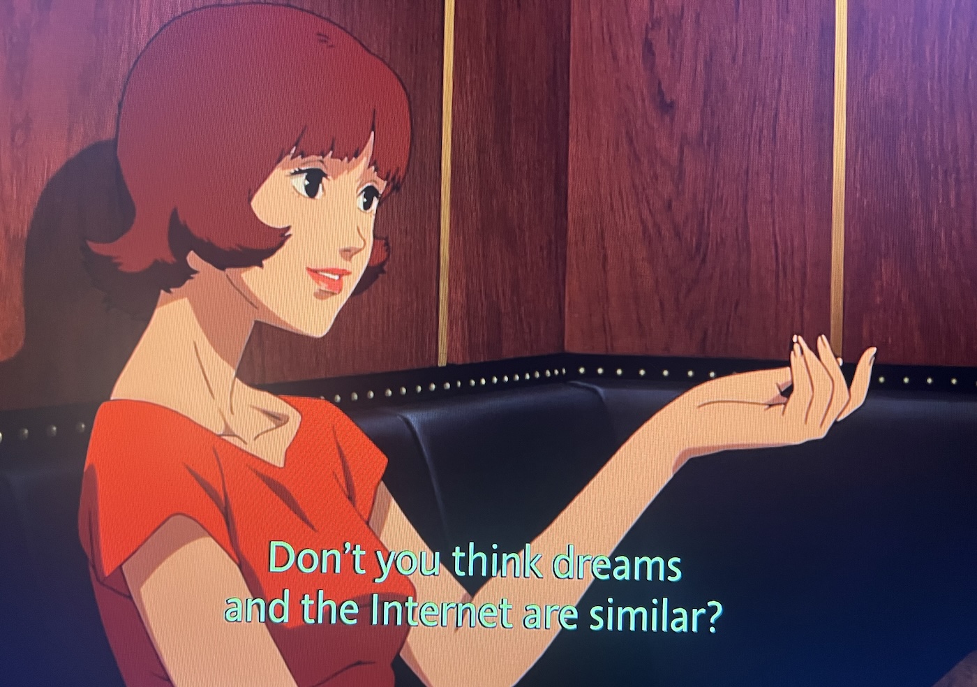 A girl sitting at a table with her hand in the air, drawn in the style of manga. The caption reads 'Don't you think dreams and the internet are similar?'
