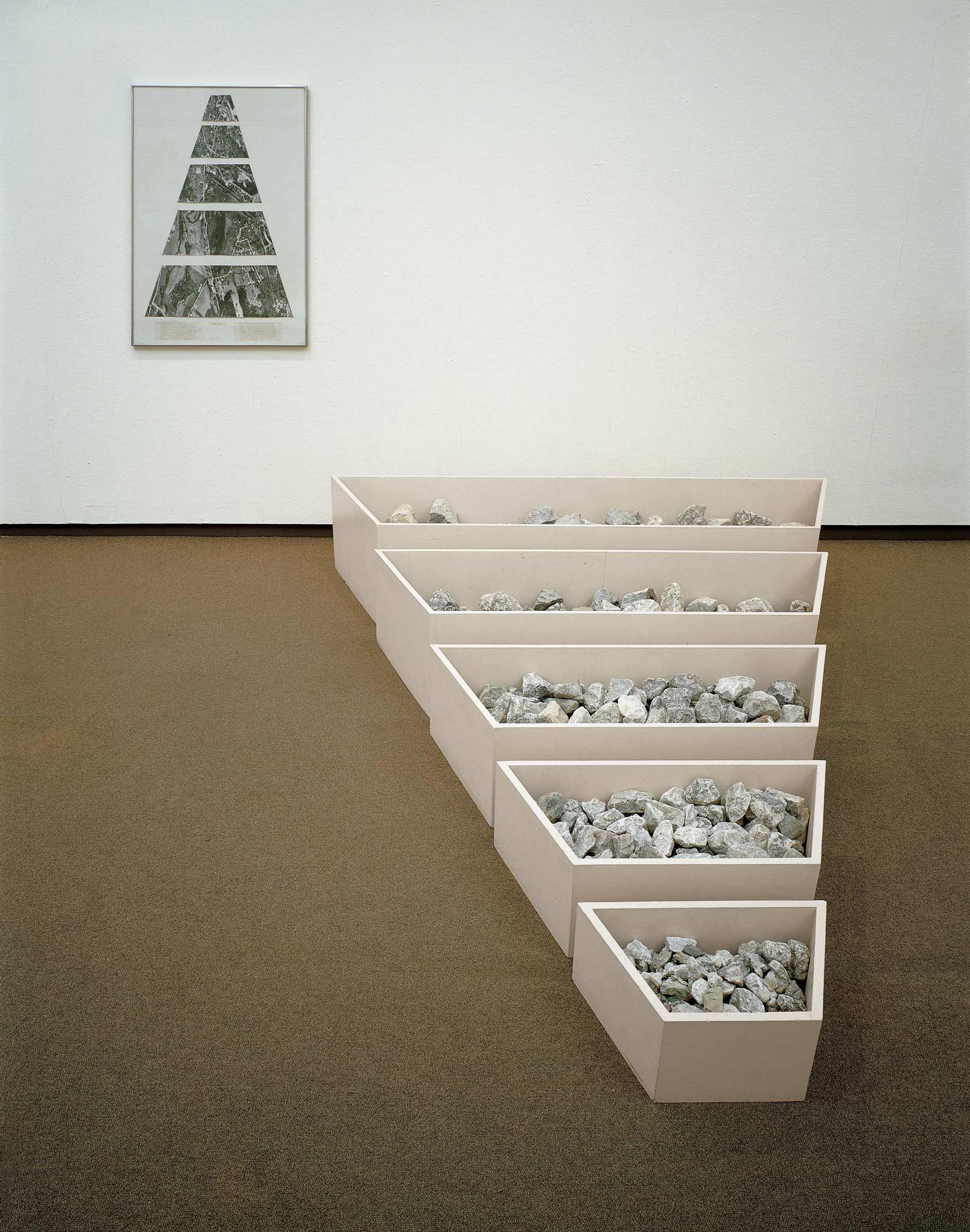 Bin-like structures in which artist Robert Smithson deposited rocks, sand, broken concrete, 
            and other elements he collected  at various sites in New Jersey. Accompanying these sculptures, Smithson hung on gallery 
            walls photographs he’d snapped at the same Garden State locations, as well as fragments of maps that could lead other people 
            to these places
