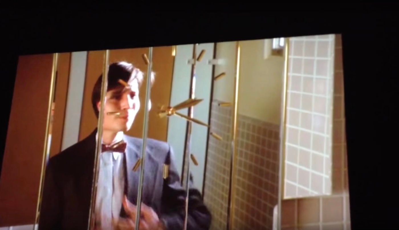 A man in a suit looking at himself in a mirror that has gold hands of a clock over it.