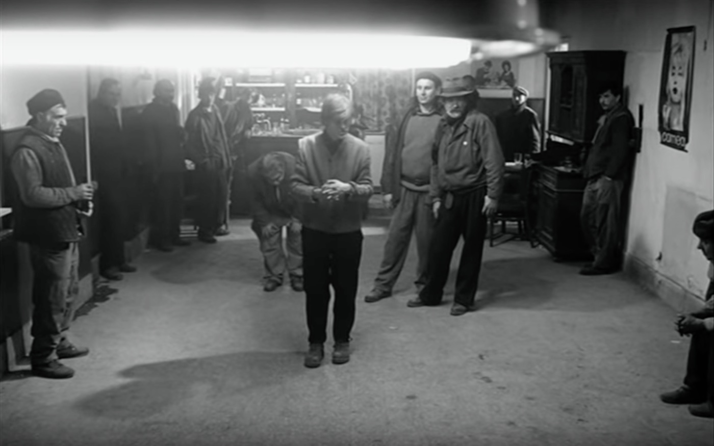 A black and white photograph of men standing in a bar with no tables or chairs visible.